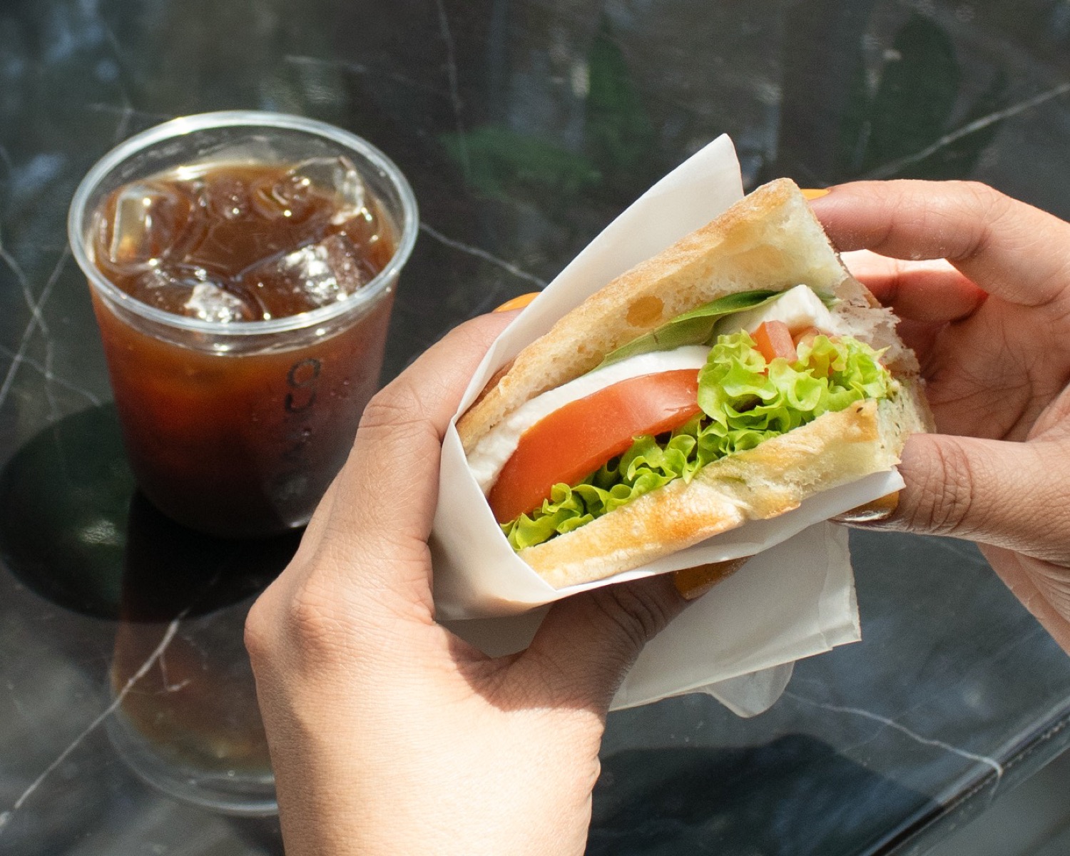 An iced coffee and a Bianco sandwich on a café table